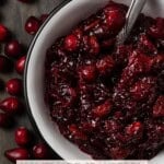 A white bowl filled with homemade cranberry sauce and a silver spoon.