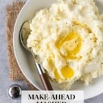 Mashed potatoes with pools of melted butter and cracked black pepper in a white bowl with a spoon, with the text "Make-Ahead Mashed Potatoes."