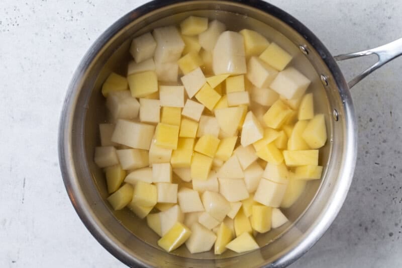 Peeled potatoes cut into small, even cubes and covered with water in a stainless steel saucepan.