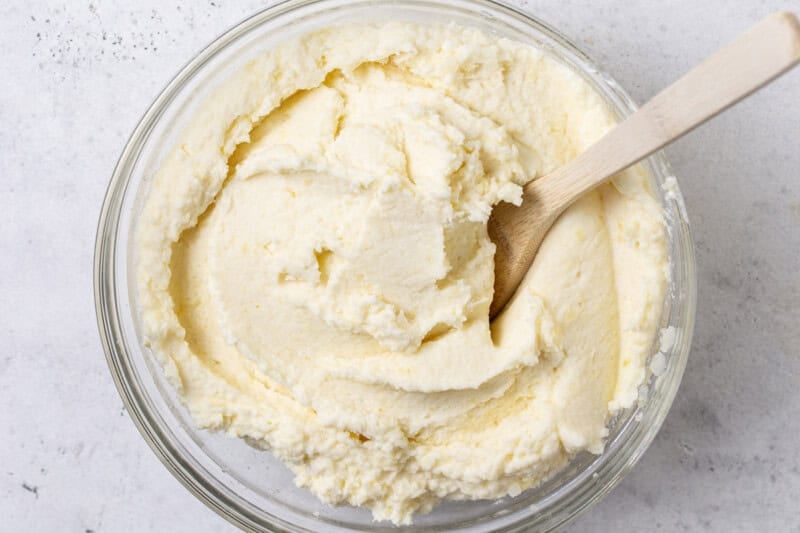 Smooth, creamy mashed potatoes in a glass bowl with a wooden spoon, mixed just until combined.