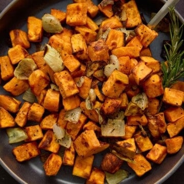A dark gray bowl filled with roasted sweet potato cubes and chopped onion.